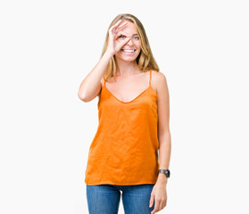 Fototapeta premium Beautiful young woman wearing orange shirt over isolated background doing ok gesture with hand smiling, eye looking through fingers with happy face.