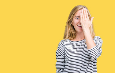 Beautiful young woman wearing stripes sweater over isolated background covering one eye with hand with confident smile on face and surprise emotion.