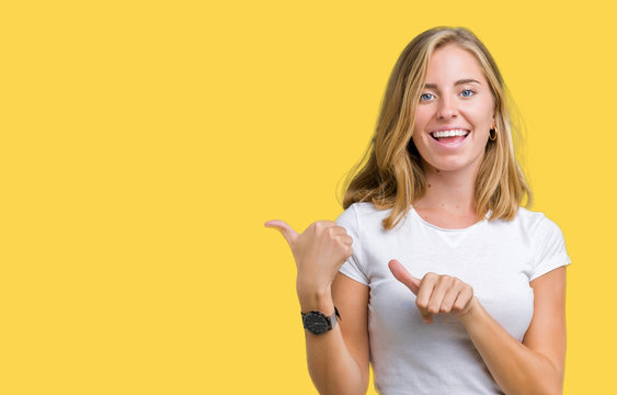 Beautiful Young Woman Wearing Casual White T-shirt Over Isolated Background Pointing To The Back Behind With Hand And Thumbs Up, Smiling Confident