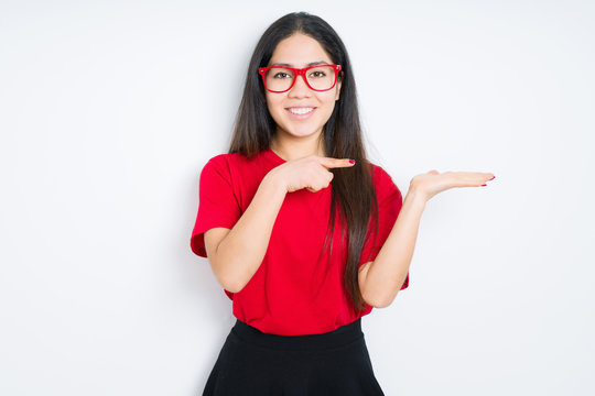 Beautiful brunette woman wearing red glasses over isolated background amazed and smiling to the camera while presenting with hand and pointing with finger.