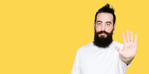 Naklejka premium Young hipster man with long hair and beard wearing casual white t-shirt doing stop sing with palm of the hand. Warning expression with negative and serious gesture on the face.