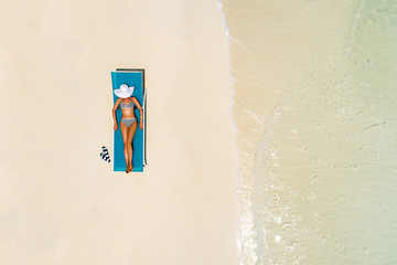 Aerial view of slim woman sunbathing lying on a beach chair in Maldives. Summer seascape with girl, beautiful waves, colorful water. Top view from drone.
