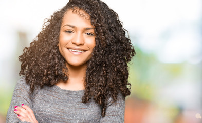 Young beautiful woman with curly hair wearing grey sweater happy face smiling with crossed arms looking at the camera. Positive person.