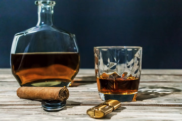 Contrast photo of a glass of whiskey, a cigar, lighter with a guillotine and a bottle of alcohol...