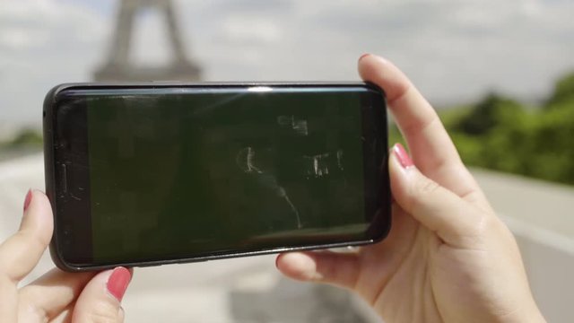 Woman using smartphone with Green Mock-up Screen at Eiffel Tower, in Horizontal Landscape Mode, watching movie, Touching touch screen. Tracking Markers. Watching Content, Videos, Blogs. Close-up.