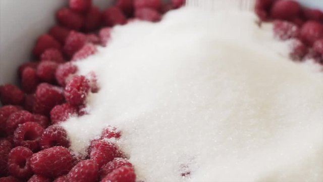 Housewife pours sugar into a bowl of raspberry jam. 