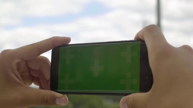 Close-up of smartphone with Green Screen at Eiffel Tower, holding by man in Horizontal Landscape Mode, watching movie on touch screen with Tracking Markers. Watching Content, Videos, Blogs.