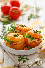 Stuffed tomatoes, baked yellow tomatoes stuffed with bulgur, vegetables and cheese with the addition of aromatic herbs in a baking dish on a white wooden table, close up. Vegetarian food