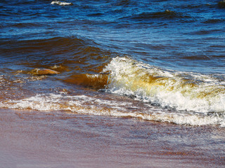 The breaking waves with foam ran to the sandy beach during a storm at the beautiful summer sea...