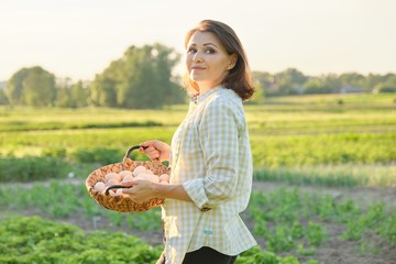 Outdoor portrait of farmer woman with basket of fresh chicken eggs, farm