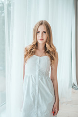 Fototapeta na wymiar Girl in a light white dress posing by the window.