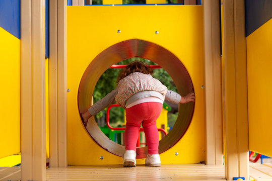 red hair little girl crawling through the tunnel in the playground