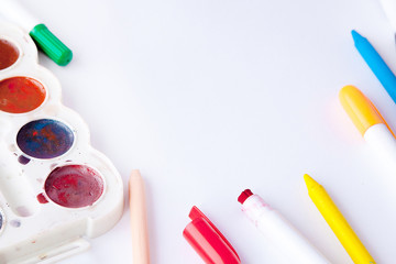 A white sheet of paper lay on a wooden table, near , pencils, paints and markers. Back to school....