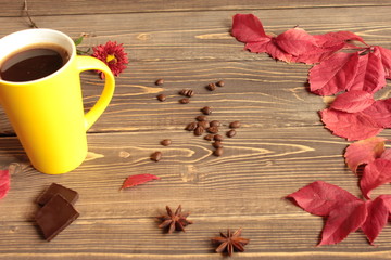 Coffee in a yellow circle, red leaves and chocolate on a wooden table.
