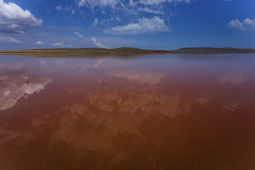The surface of the pink lake and its shore in the background. Incredible clouds are reflected in the water.