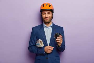 Pleased foreman wears orange helmet, elegant suit, drinks takeout coffee, carries newspaper, going on meeting with partners to discuss construction of new building. Architecture and business concept
