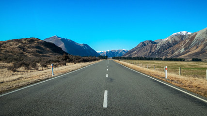 Fototapeta premium A long straight road leading towards a snow capped mountain in New Zealand.
