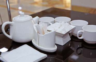 Catering - rows of cups served for tea table . Plasterboard, cutlery, toothbrush, teapot, napkin on a black glass table.