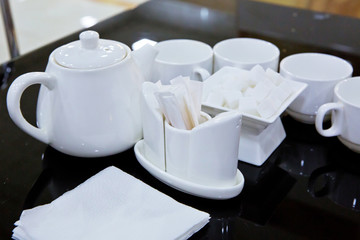 Catering - rows of cups served for tea table . Plasterboard, cutlery, toothbrush, teapot, napkin on a black glass table.