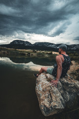 Young man enjoying the view of a mountain lake in summer. mountain reflecting in water on background.