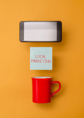 Word writing text Local Marketing. Business photo showcasing A local business where a product buy and sell in area base Coffee cup colored sticky note electronic device yolk color background