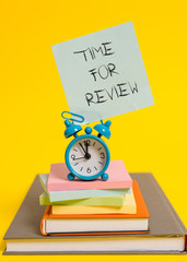Handwriting text writing Time For Review. Conceptual photo review of a system or situation in its formal examination Alarm clock note stacked notepads old books colored background