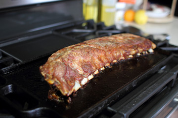 Rack of dry rub pork ribs baked on a cast iron tray, resting on the stove top.