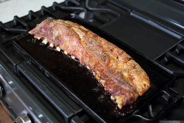 Rack of dry rub pork ribs baked on a cast iron tray, resting on the stove top.