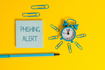 Word writing text Phishing Alert. Business photo showcasing aware to fraudulent attempt to obtain sensitive information Metal alarm clock wakeup clips ballpoint notepad colored background