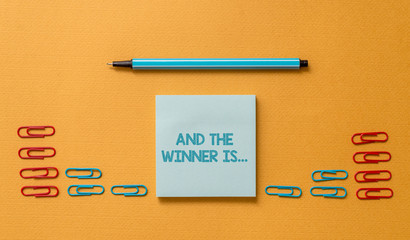 Handwriting text And The Winner Is. Conceptual photo announcing a demonstrating or thing that wins something Colored blank sticky note clips binders gathered pen trendy cool background