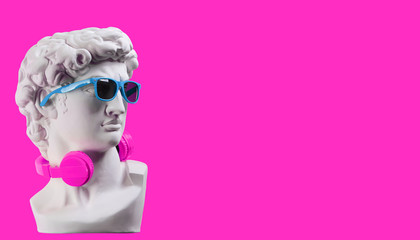Statue. Earphone on a pink background. Gypsum statue of David's head. Creative. Plaster statue of...