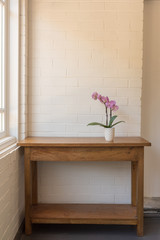 Vertical view of purple phalaenopsis orchid in pot on wooden oak side table against white painted brick wall and window (selective focus)
