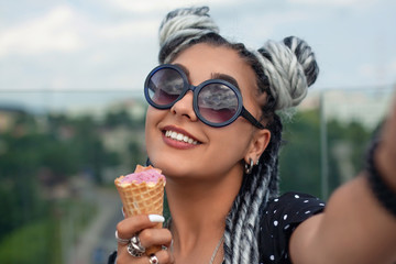 Beautiful young woman with white dreadlocks eating ice cream and taking selfie. Summer time.