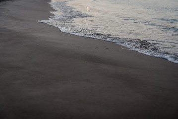 Dusk on the shore of a quiet beach while the gentle waves of the sea moisten the sand, a natural textured background.