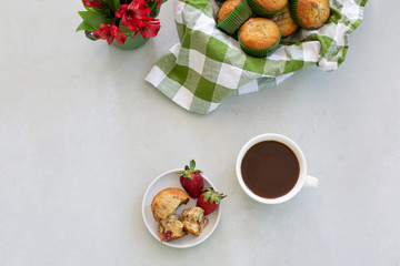 Freshly Baked Strawberry Muffins in wooden bowl with one isolated in front on plate; green and white checked cloth lining bowl; red flowers in green tin.
