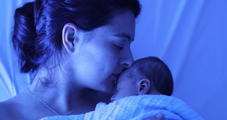 Mother holding newborn baby at hospital next to violet phototherapy lamp, real life affection and love