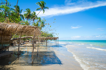 Scenic view of shallow waves lapping rustic beach shacks with palm frond palapa umbrellas on a...