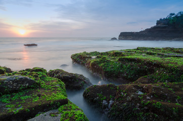 A beautiful sunset at Beach full of green moss near Tanah Lot Bali.