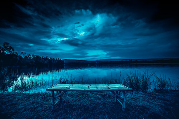 bamboo litter on grass in front of lake and moonlight behind a cloudy at night time