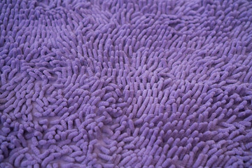 Texture of large pile floor mat. Close-up of purple fabric with soft short nap, top view. Purple textile blank background.