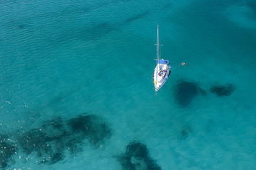 View from above, stunning aerial view of a yacht sailing on a beautiful turquoise clear water. Spiaggia La Pelosa (Pelosa beach) Stintino, Sardinia, Italy.