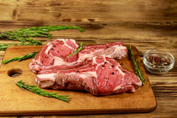 Raw fresh beef rib eye steaks on bone with spices and rosemary on wooden table