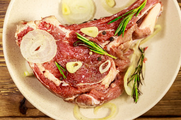 Marinated beef rib eye steak on bone with spices, onion and rosemary on wooden table