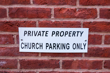 A white metal sign that says PRIVATE PROPERTY CHURCH PARKING ONLY on a brick wall