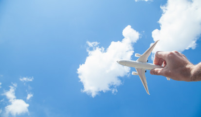 Hand holding airplane model in front of blue sky background. Travel