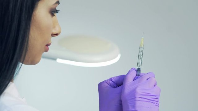Hands of the beautician in purple gloves holding syringe. Cosmetologist prepares for a injection cosmetology procedure