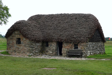 Leanach Cottage is shown preserved on the Colluden Battlefield near Inverness, Scotland. The stone foundation and thatched roof structure was likely built in the 1700s and used during battle in 1746.