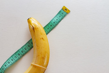 banana with condom and measure tape on white background
