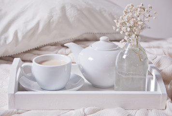 Close up of cup of tea, milk, teapot and bouquet of white flowers on the white tray.