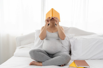 Pregnant women are reading books for their children in the belly in the white bedroom. Pregnant in the third quarter. For the development of the baby.